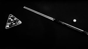 a black and white image of a rack of 8-ball and a cue laying on a pool table