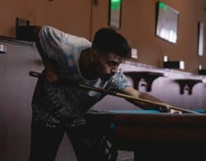 a guy shooting on a pool table up next to a wall